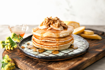 Wooden board with tasty pancakes, sliced banana and walnuts on table