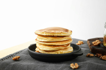 Frying pan with tasty pancakes and walnuts on table against white background