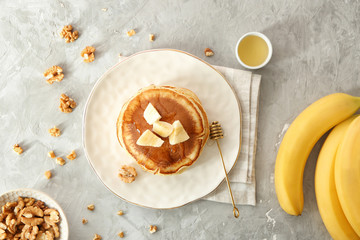 Plate with tasty pancakes, sliced banana and walnuts on grey textured background