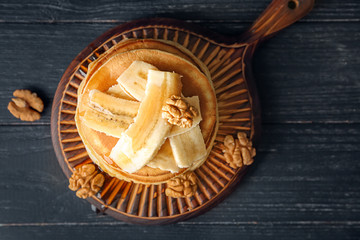 Wooden board with tasty pancakes, sliced banana and walnuts on table