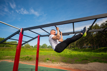 Muscular man doing pull-ups on horizontal bar outdoors. Strong athlete doing pull-up on horizontal bar.