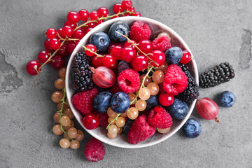 Bowl with different ripe berries on grey table