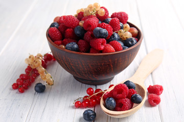 Bowl and spoon with different ripe berries on wooden table