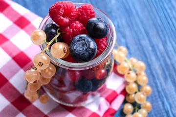Glass jar with different ripe berries on wooden table, closeup