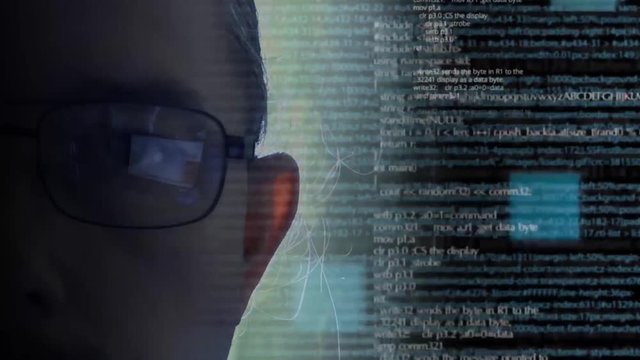 Programmer or hacker in glasses looking on monitor - software code reflecting in the glass and flying around. Caucasian man face in the dark. Digital technologies.