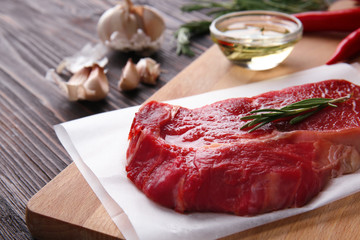 Wooden board with raw meat and rosemary on wooden table, closeup