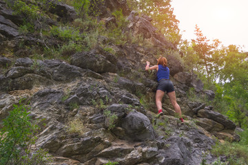 Young red-haired girl climber in sports clothes climbs on rocks to the top in mountains of Altai without equipment and insurance