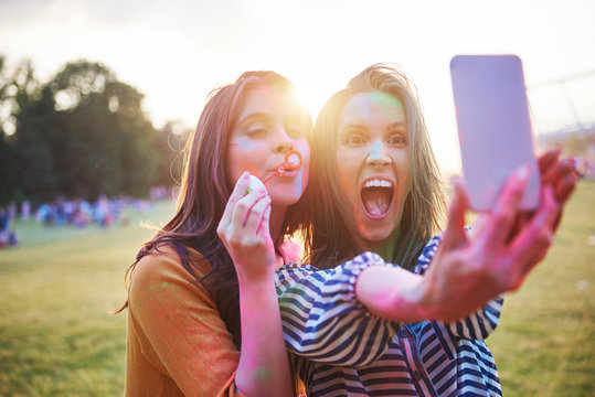 Two young woman covered in coloured chalk powder taking selfie at Holi Festival