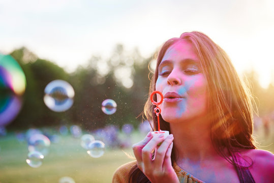 Young woman covered in coloured chalk powder blowing bubbles at Holi Festival