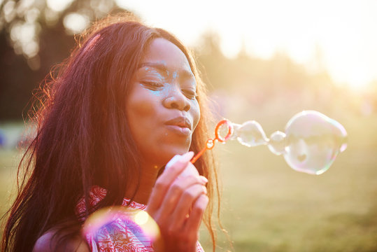 Young woman covered in coloured chalk powder blowing bubbles at Holi Festival