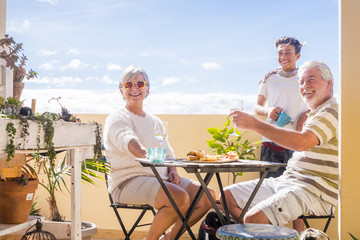 grandfathers adult mature and teenager nephew enjoy outdoor in the terrace some leisure with food and drinks. ocean and city view, vacation sunny day nice weather concept and background. happy people - obrazy, fototapety, plakaty