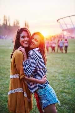 Two young women covered in coloured chalk powder hugging at Holi Festival, portrait