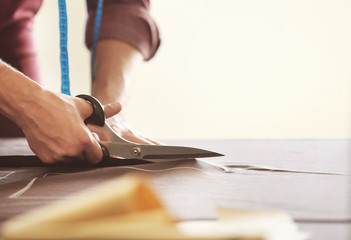 Young tailor cutting fabric in atelier, closeup