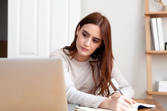 Woman writing notes into notepad from laptop