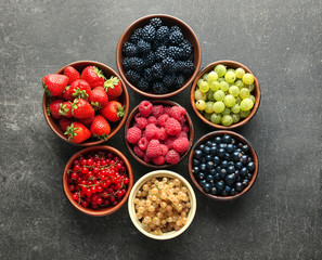 Bowls with various ripe berries on grey background, top view