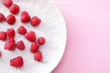 Plate with sweet ripe raspberries on color wooden table