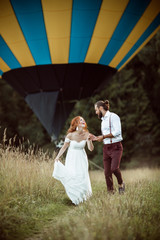 Happy lovely couple bride and groom are walking near airballoon basket in the field, wedding and adventure concept
