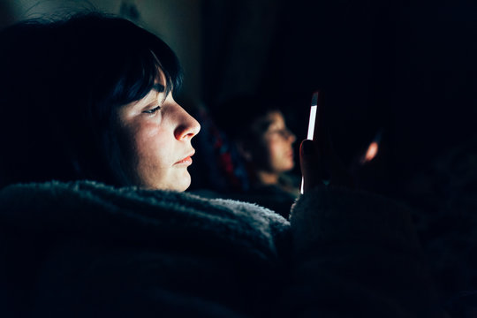 Women in bed in darkness using mobile phones
