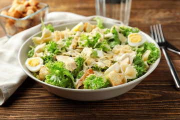 Tasty Caesar salad with pasta in bowl on wooden table