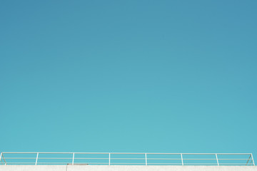 Imagen minimalista de un balcón, azotea con una valla blanca bajo un cielo azul despejado