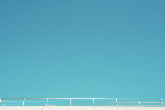 Imagen minimalista de un balc&oacute;n, azotea con una valla blanca bajo un cielo azul despejado