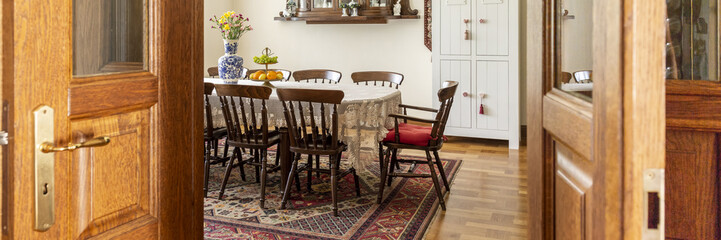Wooden chair at table with flowers in classic dining room interior with patterned carpet. Real photo