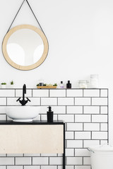 Round mirror above white cabinet in simple bathroom interior. Real photo