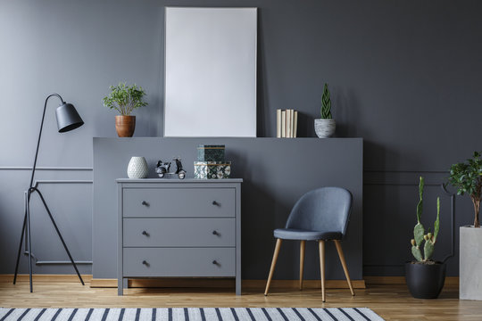 Grey cabinet between black lamp and chair in living room interior with mockup of poster. Real photo