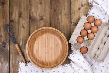 Preparation of homemade cakes on a wooden background. Ingredients and accessories for the kitchen and at home. Bowl, eggs and space for text. Top view