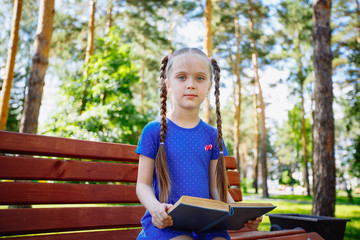 Cute little girl is reading a book outdoors