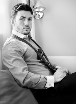 Handsome businessman wearing tie and open shirt sits in front of window of hotel room