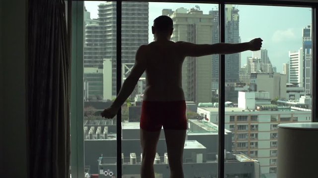 Man walking in his apartment in underwear and stretching muscles
