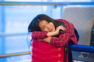 Obraz premium young beautiful and happy Asian Korean tourist woman with travel suitcase in airport sitting at departures lounge gate waiting for flight smiling cheerful