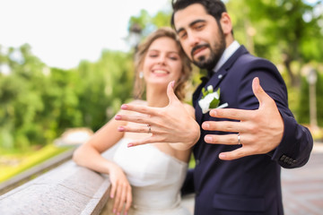 Happy newlyweds showing their wedding rings outdoors - obrazy, fototapety, plakaty