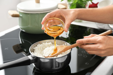 Woman adding oil to boiled rice in saucepan, closeup