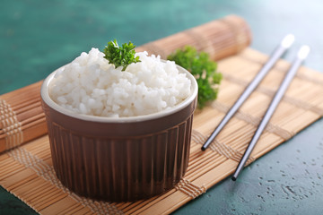 Bowl with boiled white rice and chopsticks on bamboo mat