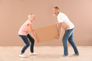Mature couple with box near color wall indoors. Moving into new house