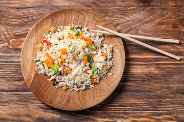Plate of tasty rice with vegetables and chopsticks on wooden table