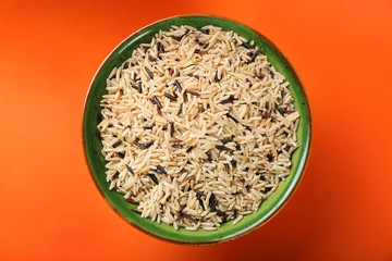 Bowl with raw rice on color background