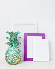Wooden empty frames for a photo and wooden emerald pineapple on a background of a white wall. Blank paper frames, modern home decor mock-up. Interior accessories, home decor elements.