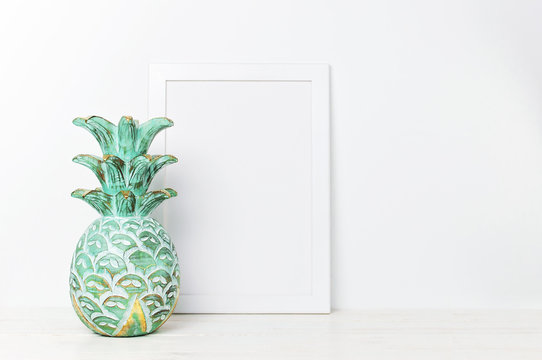 Wooden empty frames for a photo and wooden emerald pineapple on a background of a white wall. Blank paper frames, modern home decor mock-up. Interior accessories, home decor elements. 