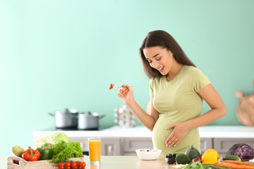 Young pregnant woman eating fresh vegetable salad in kitchen
