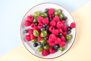 Plate with delicious ripe berries on color background