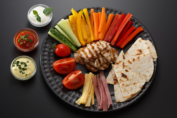 Pieces of tortillas with different sauces, vegetables, meat and cheese on a black plate on a black background.