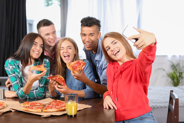 Young people taking selfie at party with delicious pizza indoors