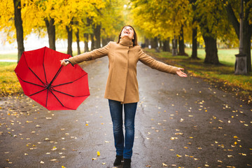 Obraz premium Happy woman with red umbrella walking at the rain in beautiful autumn park.