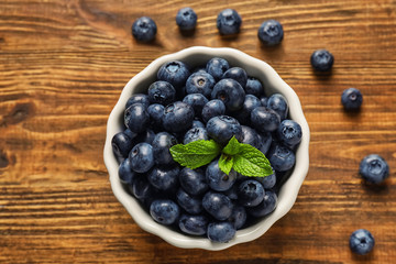 Bowl with ripe blueberries on wooden background
