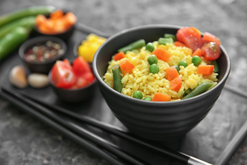 Bowl with tasty boiled rice and vegetables on grunge table, closeup