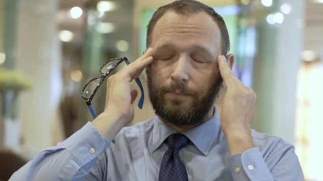 Businessman sitting in the cafe and having painful headache
