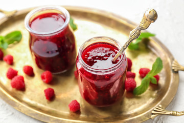 Jars with tasty raspberry jam on metal tray